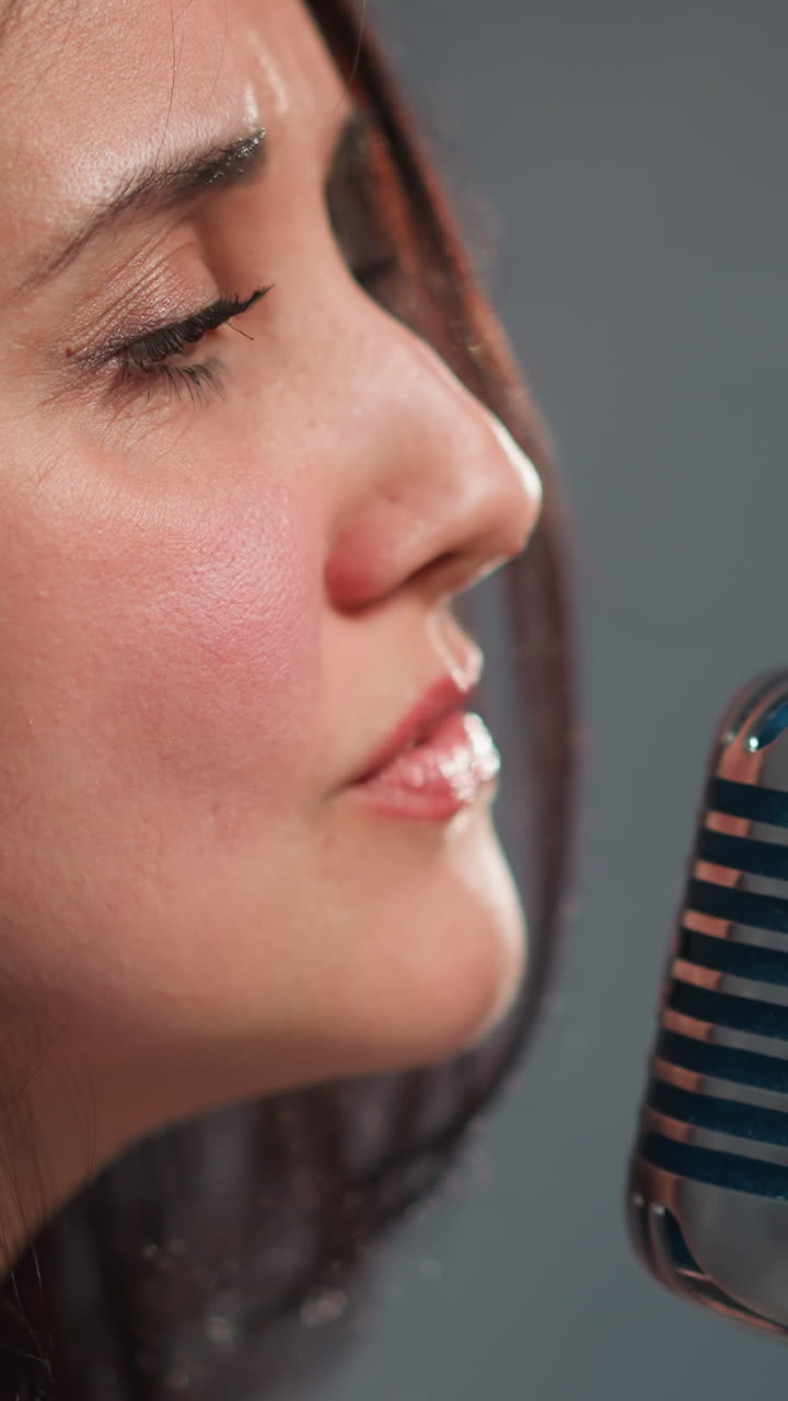 cantante emocional femenina en una chaqueta de cuero y una camiseta de pañuelos actuando en un micrófono vintage contra un fondo blanco