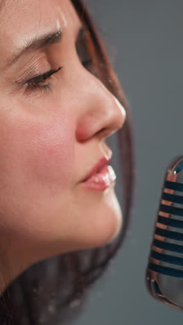 cantante emocional femenina en una chaqueta de cuero y una camiseta de pañuelos actuando en un micrófono vintage contra un fondo blanco