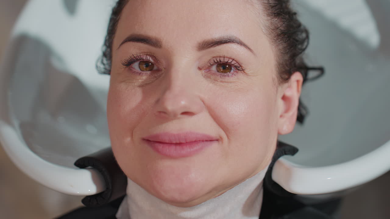 Mulher desfrutando de cuidados com o cabelo, mulher relaxando durante tratamento de salão de beleza, mulher sentada recebendo uma experiência suave de lavagem de cabelo, mulher sorrindo tranquilamente enquanto a equipe do salão enxágua suavemente a sequência do cabelo