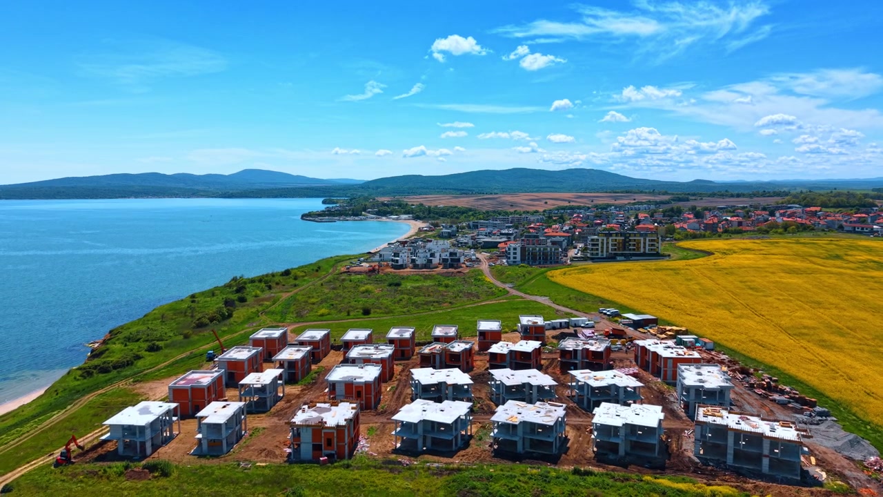 Yapım aşamasındaki sahil evleri projesinin havadan manzaralı panoraması. Mavi denizin ve sarı çiçek tarlasının yanında inşa edilen yeni bir konut tatil köyünün havadan görünümü.