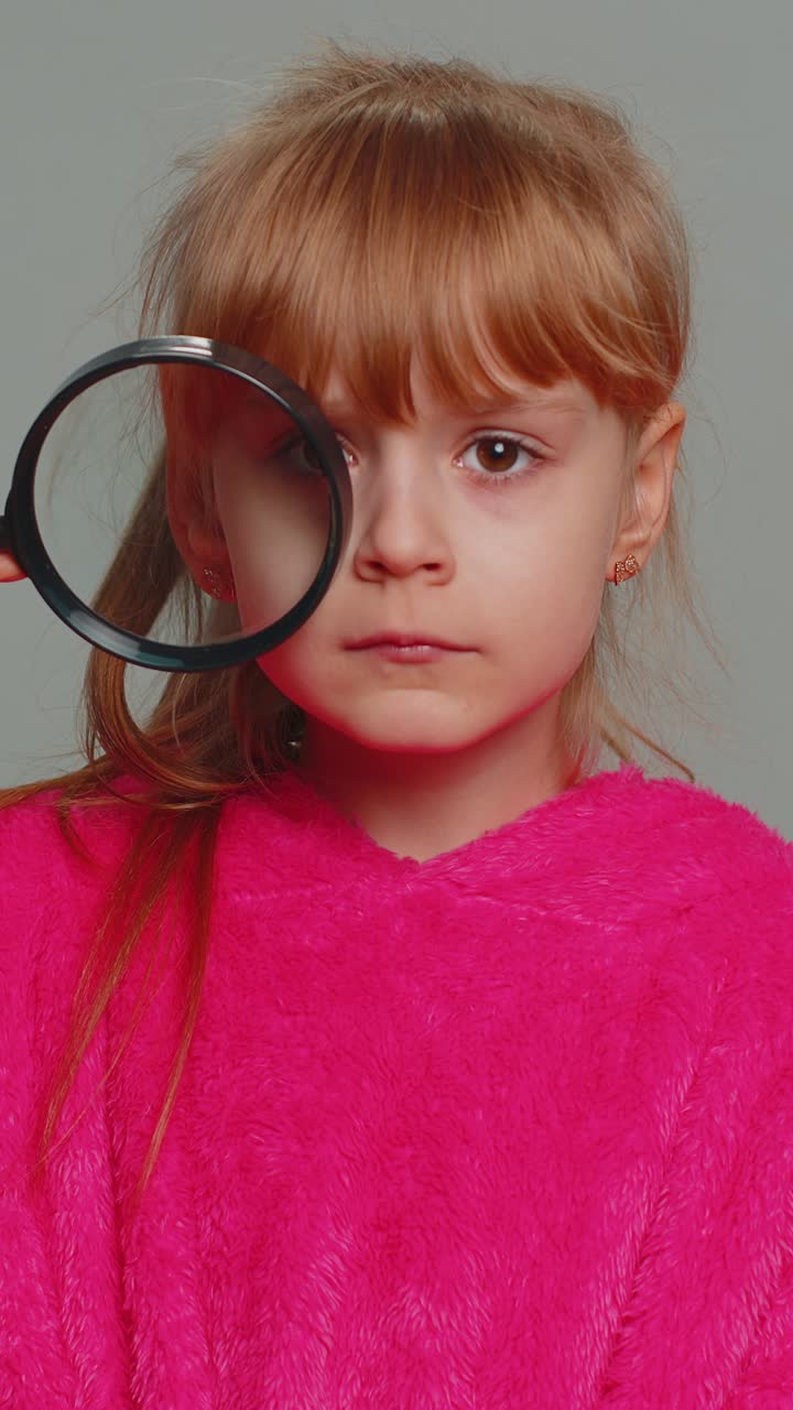 Bambina preadolescente curiosa con una lente d'ingrandimento vicino al viso, con un occhio divertito che cerca e analizza.