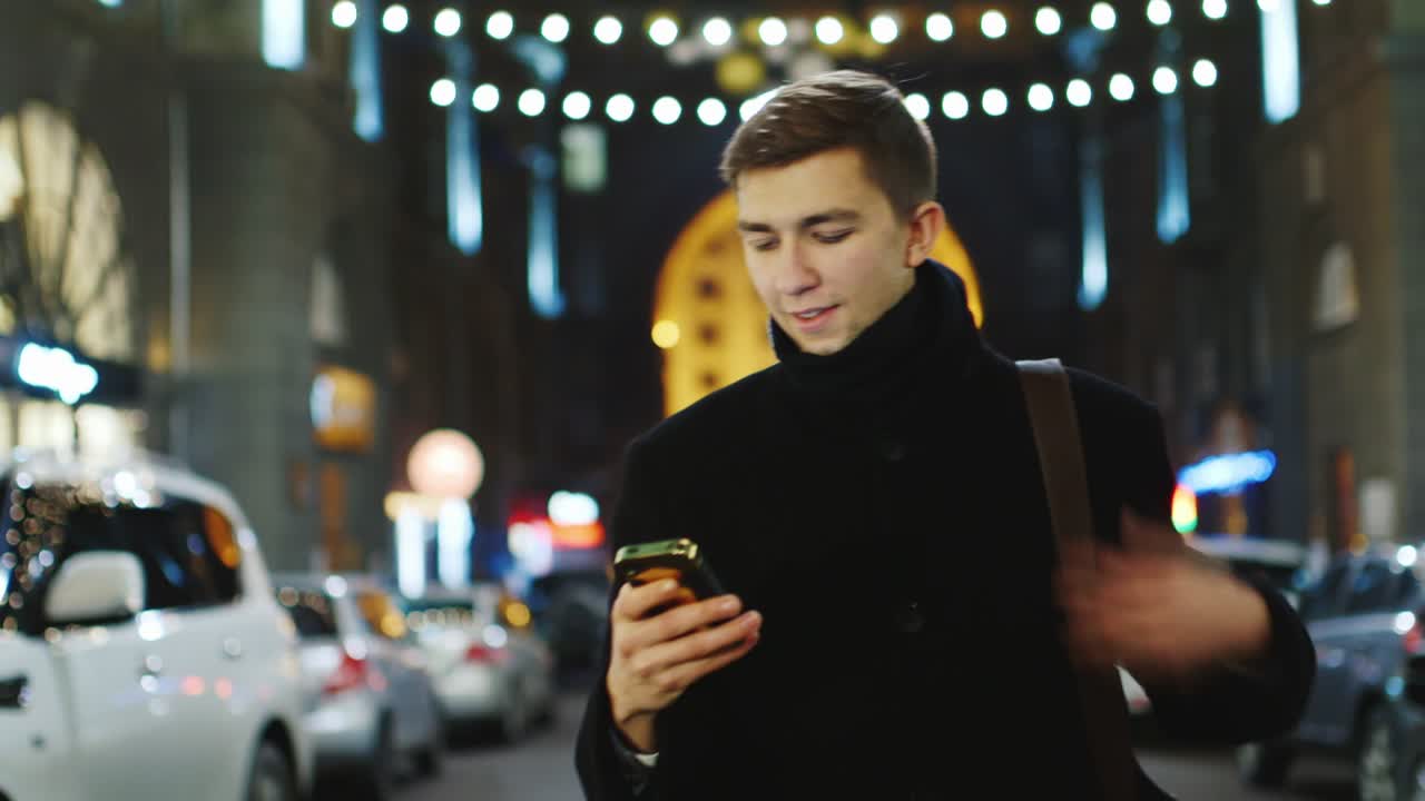 un joven camina por la ciudad nocturna y usa un teléfono inteligente 1