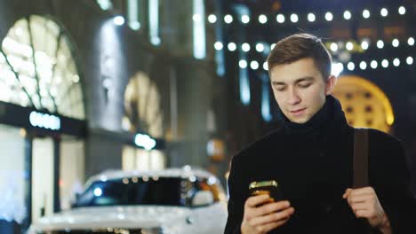 A-young-man-walks-through-the-night-city-and-uses-a-smartphone-1