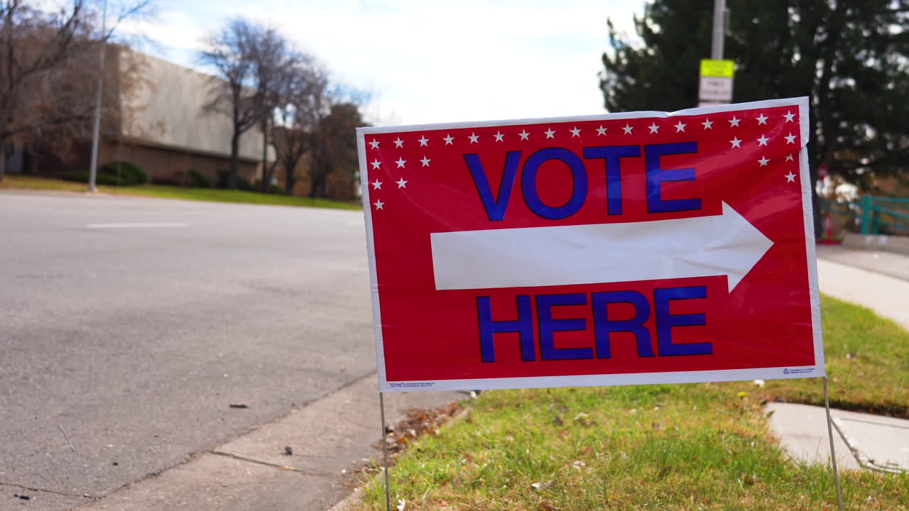Vote Here Sign Pointing Right Next to Empty Road, Close Up