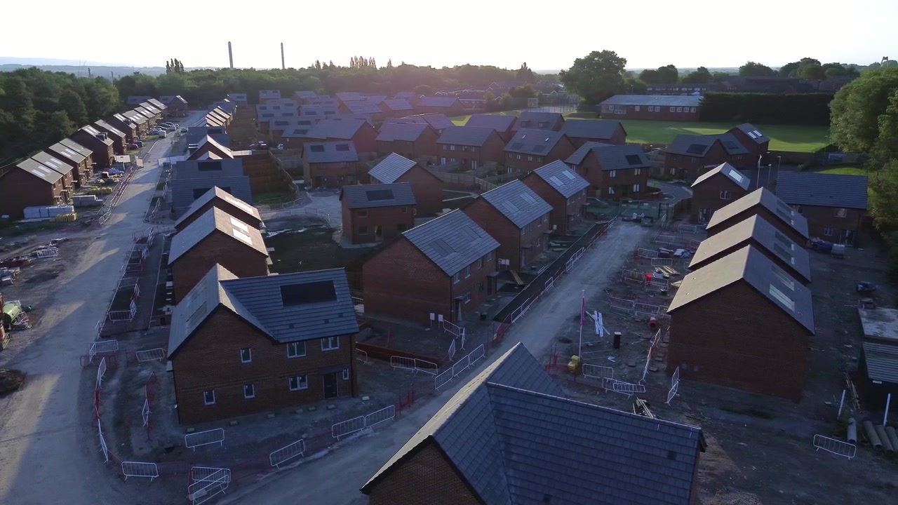 Luftfoto af ufærdig råhusbyggeplads til nyt hjem over et udbygningsområde ved solopgang.