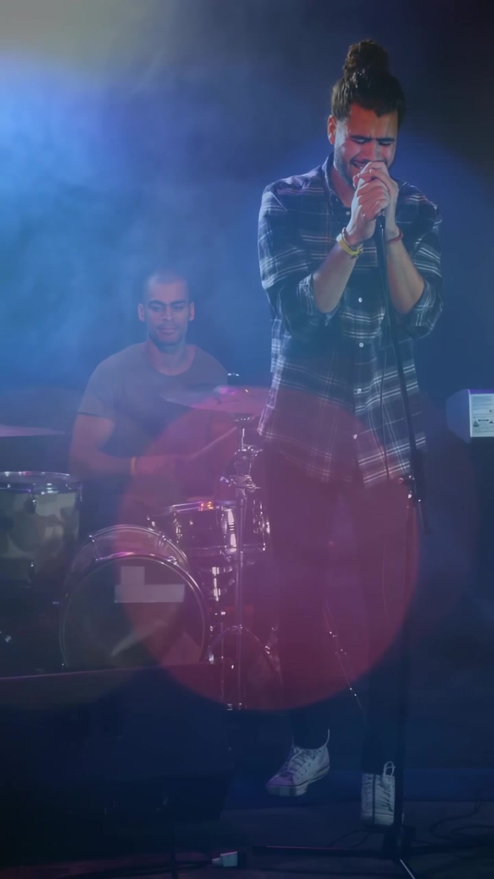 Video verticale: Cantante che inizia una strofa, afferra il microfono, batterista che tiene il ritmo, esprimendo l'emozione della musica.