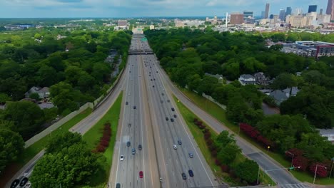 traffic on multi lane highway in atlanta surrounded. by green trees in summer. aerial wide shot. left side suburb district, right side downtown skyline. georgia, united states