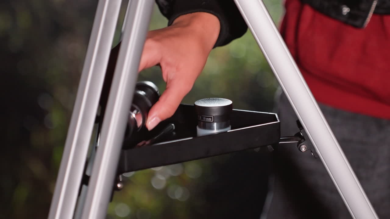 closeup telescope tripod tray with eyepiece, amateur astronomer adjusts eyepiece on mount during nighttime backyard observation, hands place and tighten lens, metal knob turned for focus, soft bokeh