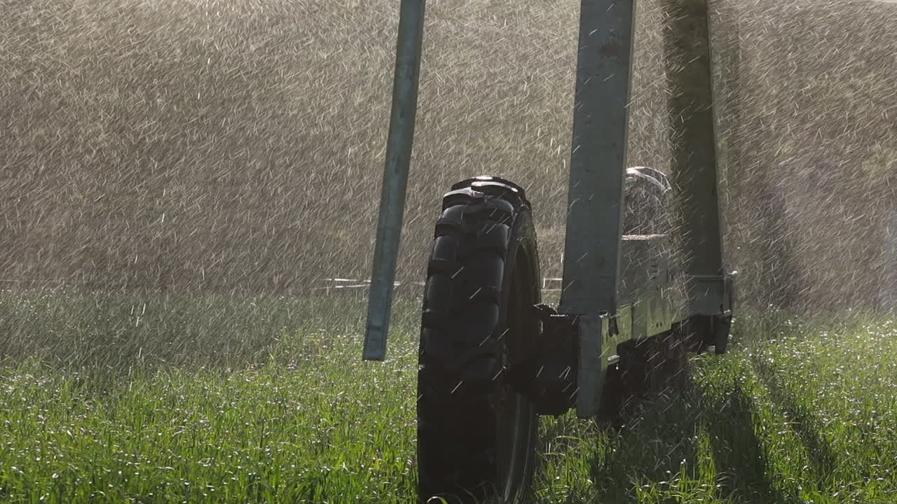 Baggrundsbelyst sprøjtetåge væder hjulene på en vandingspivot i en grøn afgrødemark.