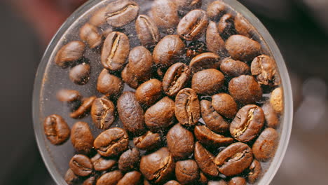 A-close-up-view-of-coffee-beans-being-poured-into-the-bottom-of-a-glass-cup