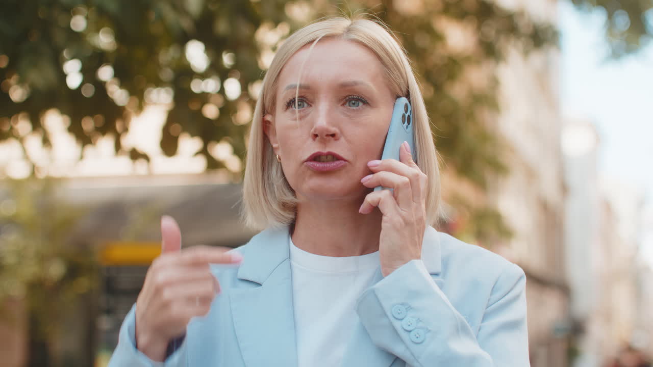 mujer de negocios caucásica madura enojada discutiendo mientras habla en teléfono inteligente de pie en la calle de la ciudad