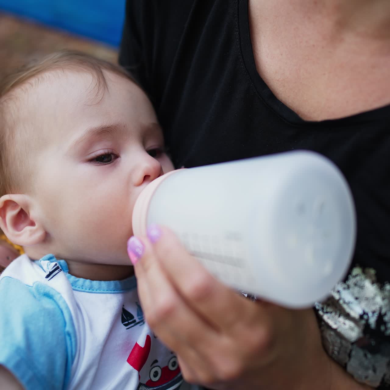 Sweet baby suckling milk from bottle. Lovely child lying in mom's hands and having some meals. Close up
