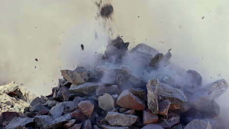 tirar un montón de piedras en un sitio de construcción en cámara lenta aislada con polvo y escombros volando por todas partes