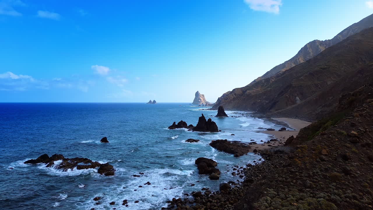 Rocky coast of the Atlantic Ocean with a narrow line of sandy beach. Drone footage at the shore of Tenerife, the Canary Islands, Spain