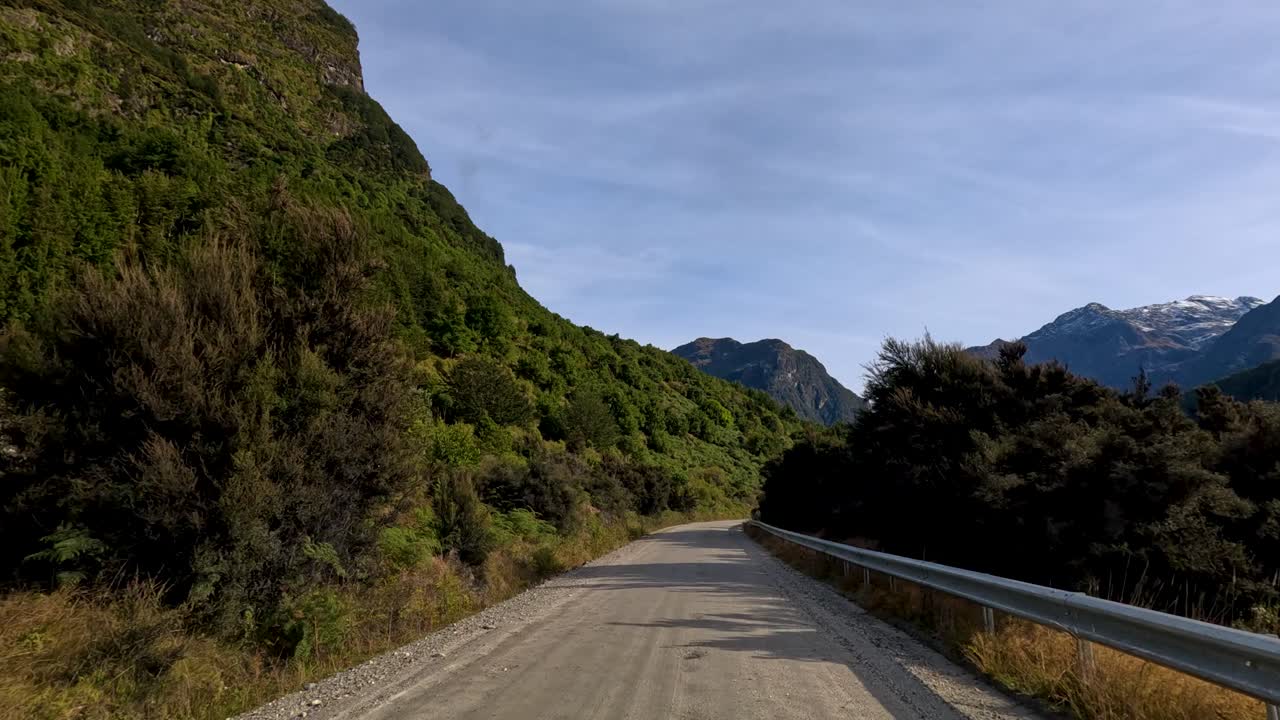 Vehicle travels gravel road, lush green mountains, clear daylight, steady forward camera, scenic landscape