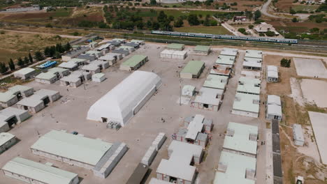 imágenes de rotación aérea de un campamento de inmigrantes en bari, italia, con trenes de pasajeros pasando al fondo