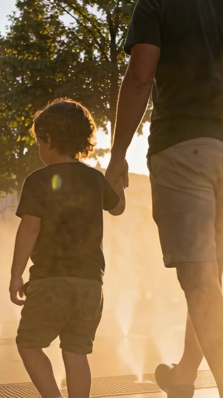 Vídeo vertical: Vendo jatos, pai caminhando guiando criança de mãos dadas através da névoa no parque, de shorts