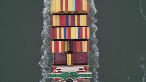 a top down view directly above a large, red container ship with red and yellow containers on the hudson river on a cloudy day