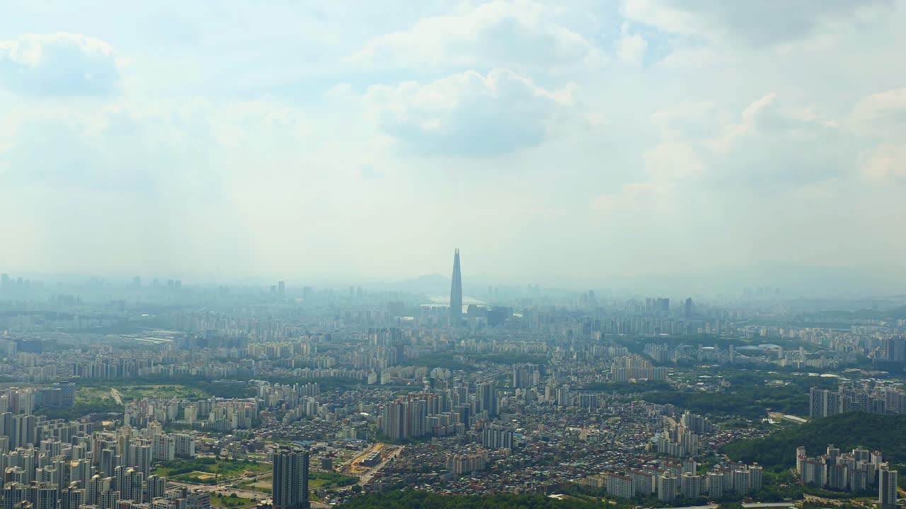 A slow zoom-out shot reveals the vast, sprawling metropolis of the Seoul cityscape in South Korea, with the iconic Lotte World Tower standing tall on a hazy summer day