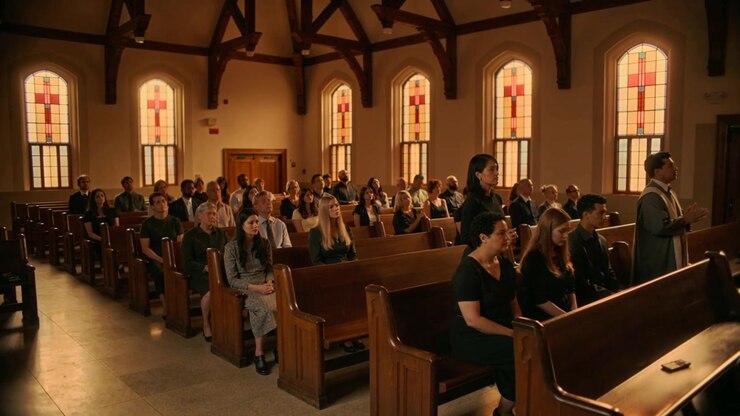 Rising woman in dark clothing walking to front at church after shifting in pews, phone visible