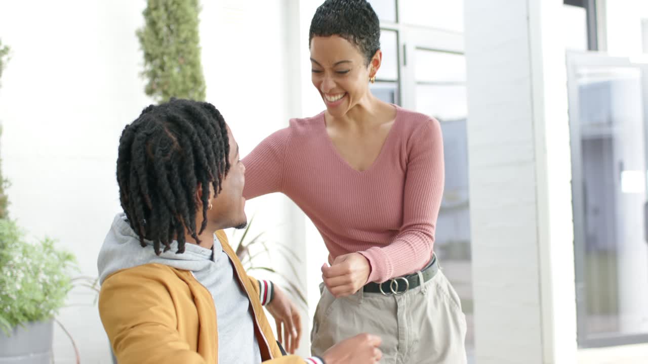 Diverse couple hugging on home patio after woman tapping man's shoulder causing joyful surprise