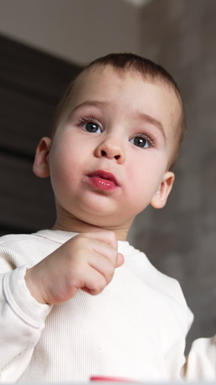 Lovely Caucasian kid sitting at the feeding table. Baby boy taking the pieces of food from plate and putting them into mouth. Low angle view close up. Vertical video