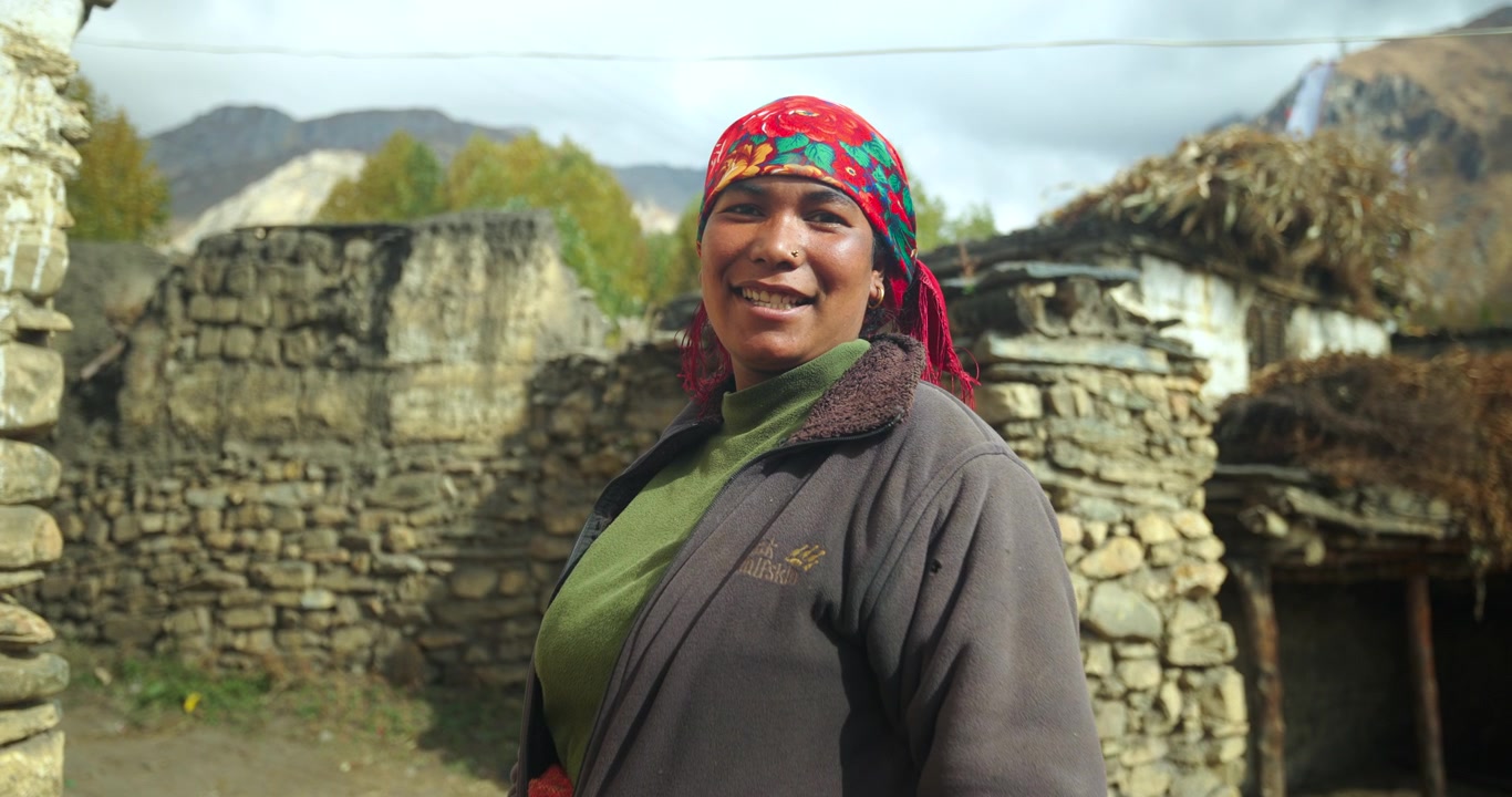 Annapurna Circuit, Mustang Nepal, close up aerial shot of a joyful local woman wearing a red headscarf against traditional stone houses.