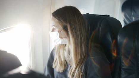 Woman-in-protective-mask-on-plane-looking-to-window