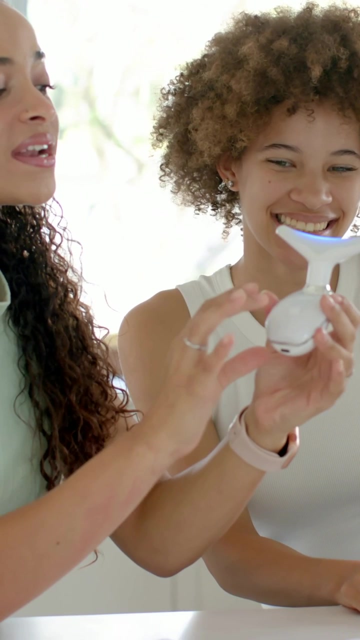 Video verticale: Donne che si passano un dispositivo LED blu sul bancone di casa, una donna in verde che prende una maschera.