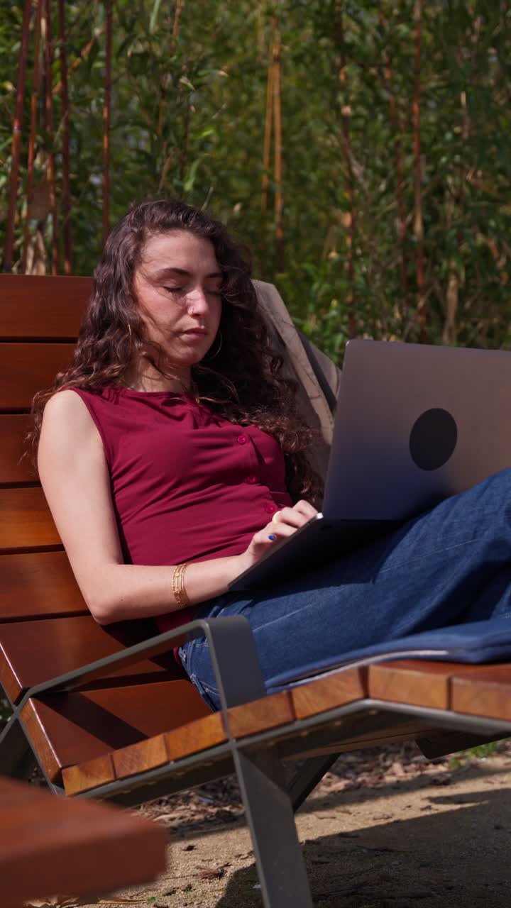 Giovane donna che lavora al laptop all'aperto in un parco soleggiato.