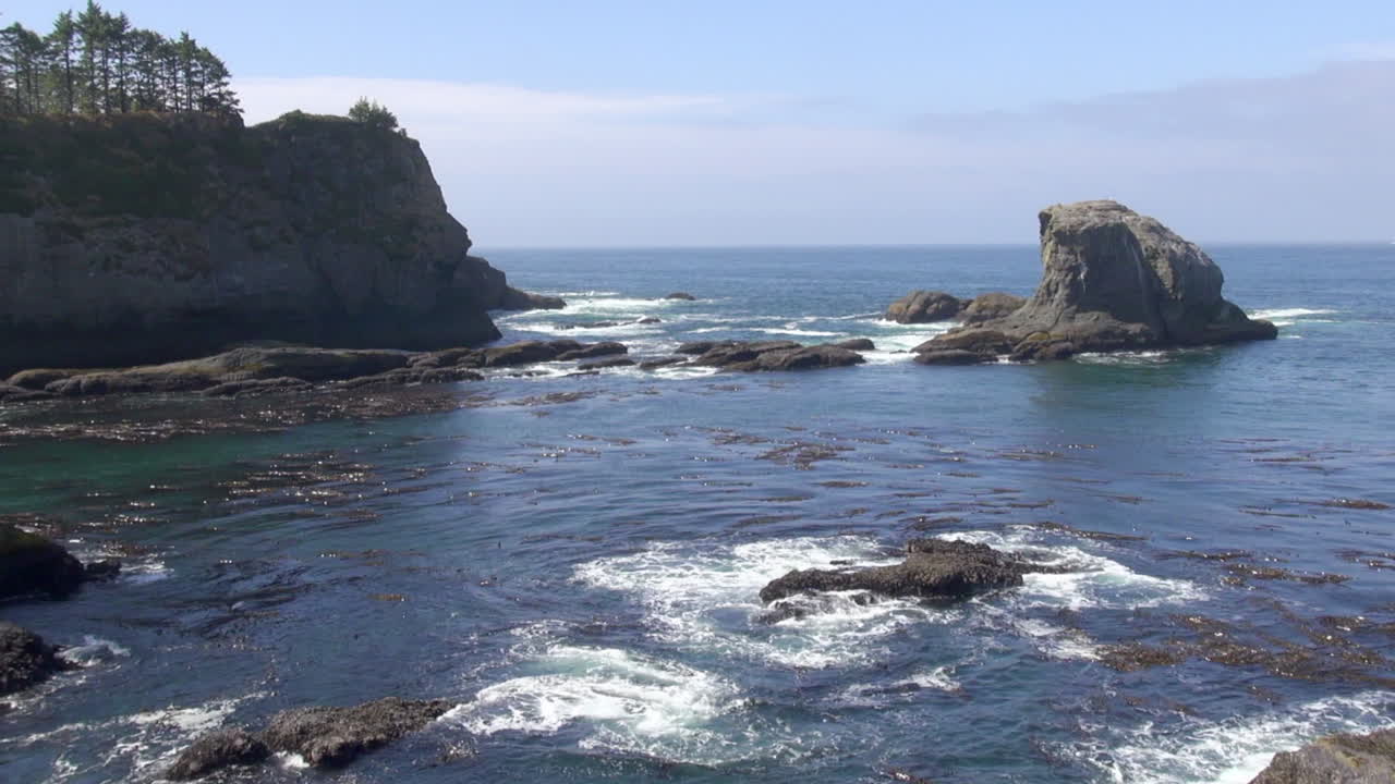Pacific ocean waves wash over low rocky islets near inlet kelp beds