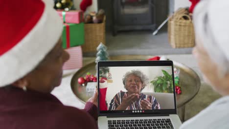 sonriendo diversas amigas mayores usando una computadora portátil para una videollamada de navidad con una mujer en la pantalla