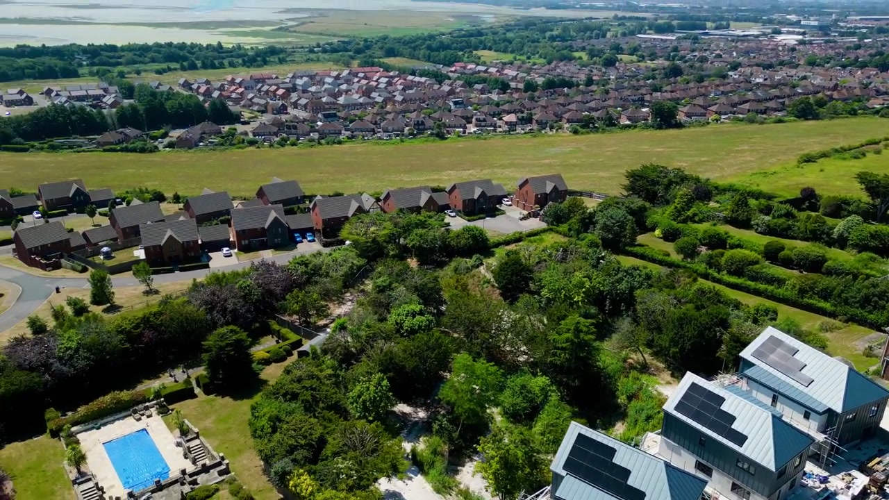 Aerial drone shot of Portsdown Hill revealing suburban housing, hillside greenery, open countryside and distant coastline during daytime in Portsmouth, England, United Kingdom
