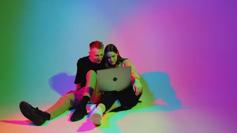 modern young teen girl and boy with laptop watching movies, series, playing or shopping online. colorful neon light