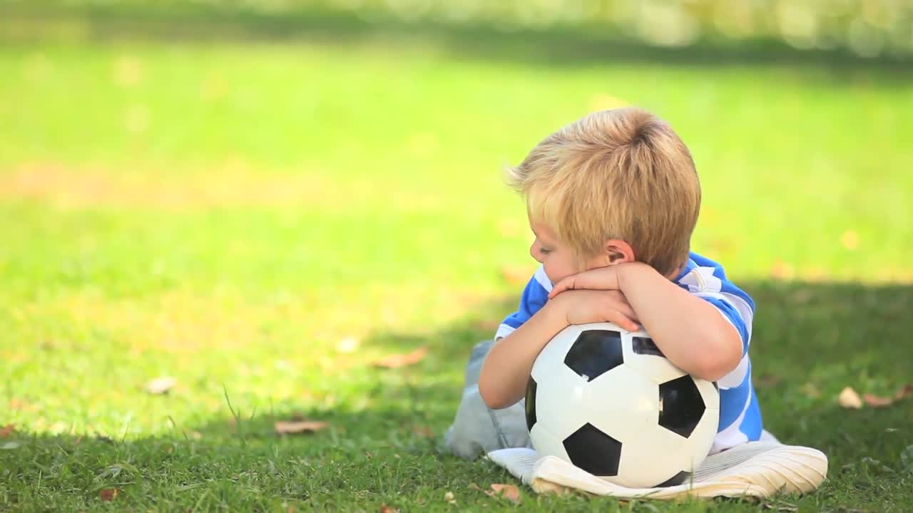 Menino deitado na grama com sua bola