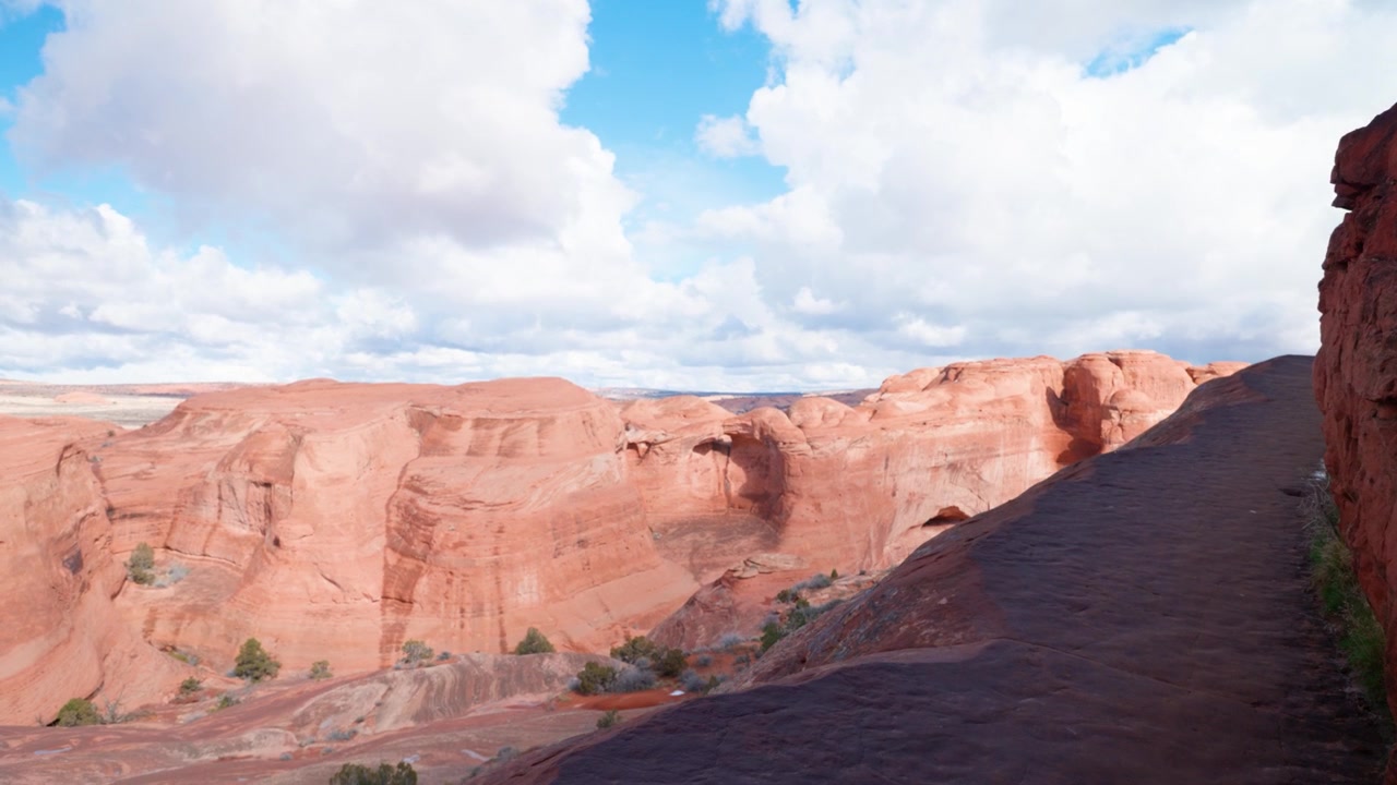 Indzoomende skud, der følger en smal vandresti mod kanten af en klippe i Arches National Park, Utah, på en solrig dag.