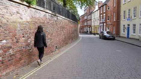 wide shot following an attractive young woman down a cobble street