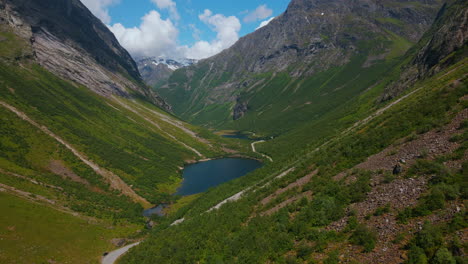 drone flies to its left and reveals a lake in the valley with high mountains and steep hills