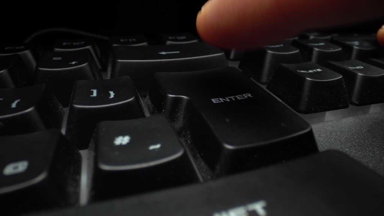 Finger pressing enter button on a black computer keyboard.
