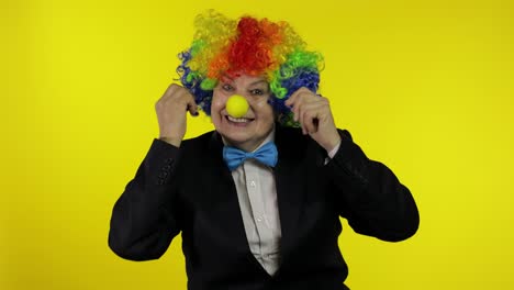 senior old woman clown in colorful wig smiling, making silly faces, fool around