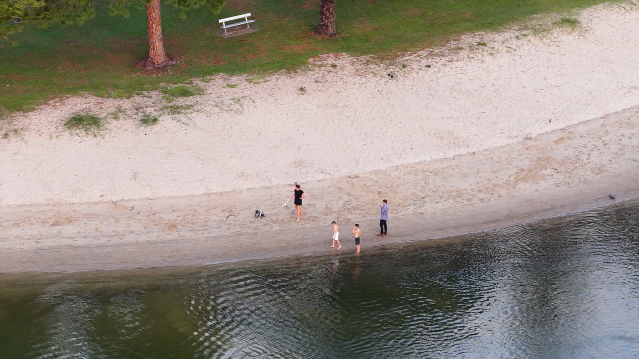 Overhead drone shot of people and dogs walking on sandy canal bank in soft daylight