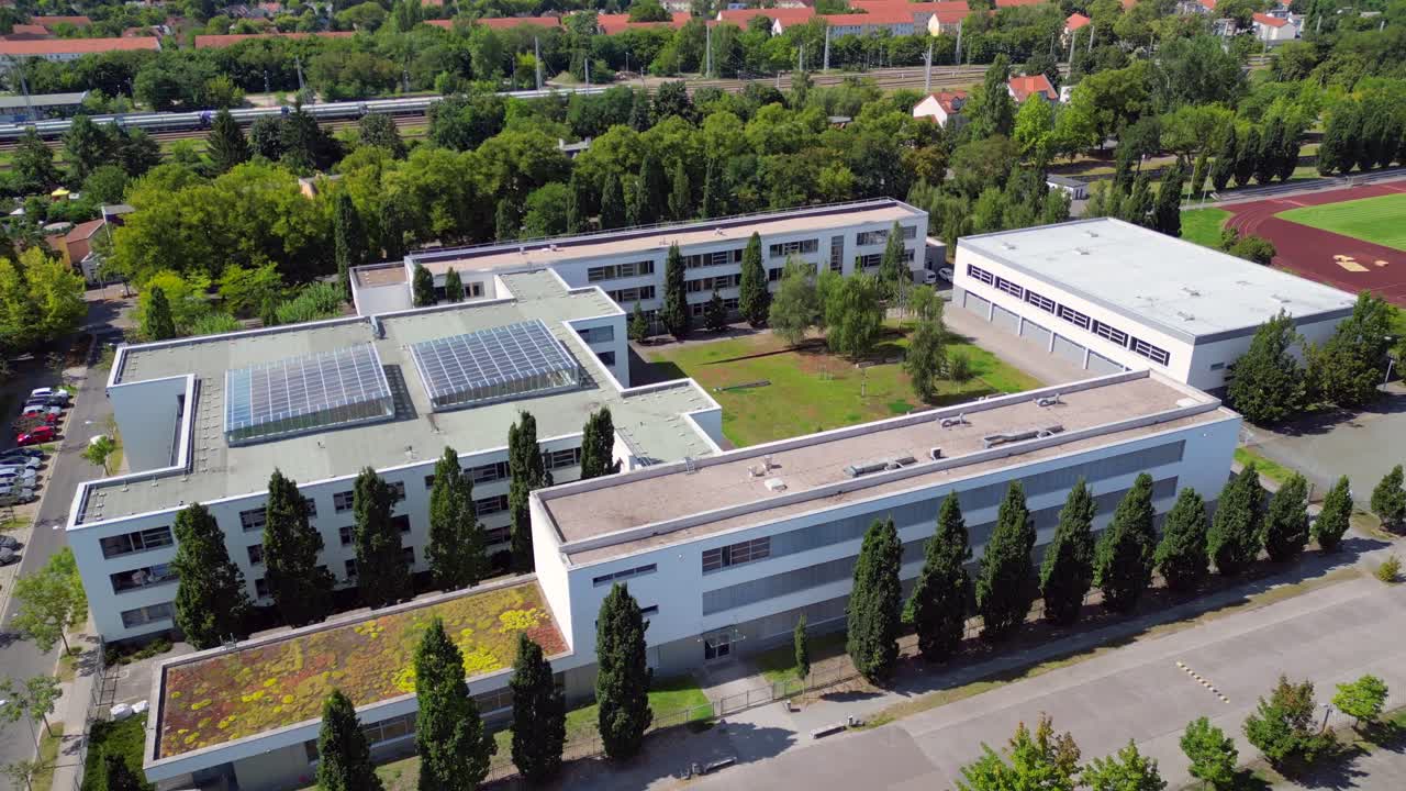 Hennigsdorf High School showcasing its modern architecture, sports facilities, parking area, surrounding urban landscape. Dramatic aerial view flight ascending drone