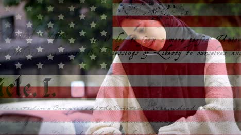 animation of american flag waving over mixed race woman in hijab talking on her smartphone