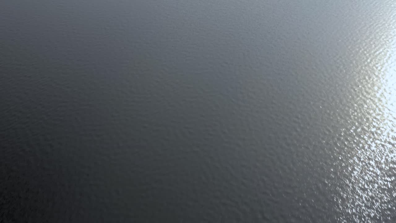Drone flying low and fast along surface of rippled water with sunlight reflections
