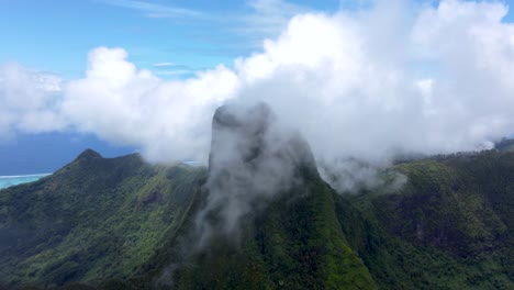 drone view of a green tropical pacific mountain peak surrounded by clouds on a sunny day in mouaputa, moorea, french polynesia.