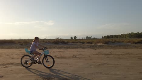 little girl riding a bicycle on a sandy road as the sun shines at dusk, catalonia, spain