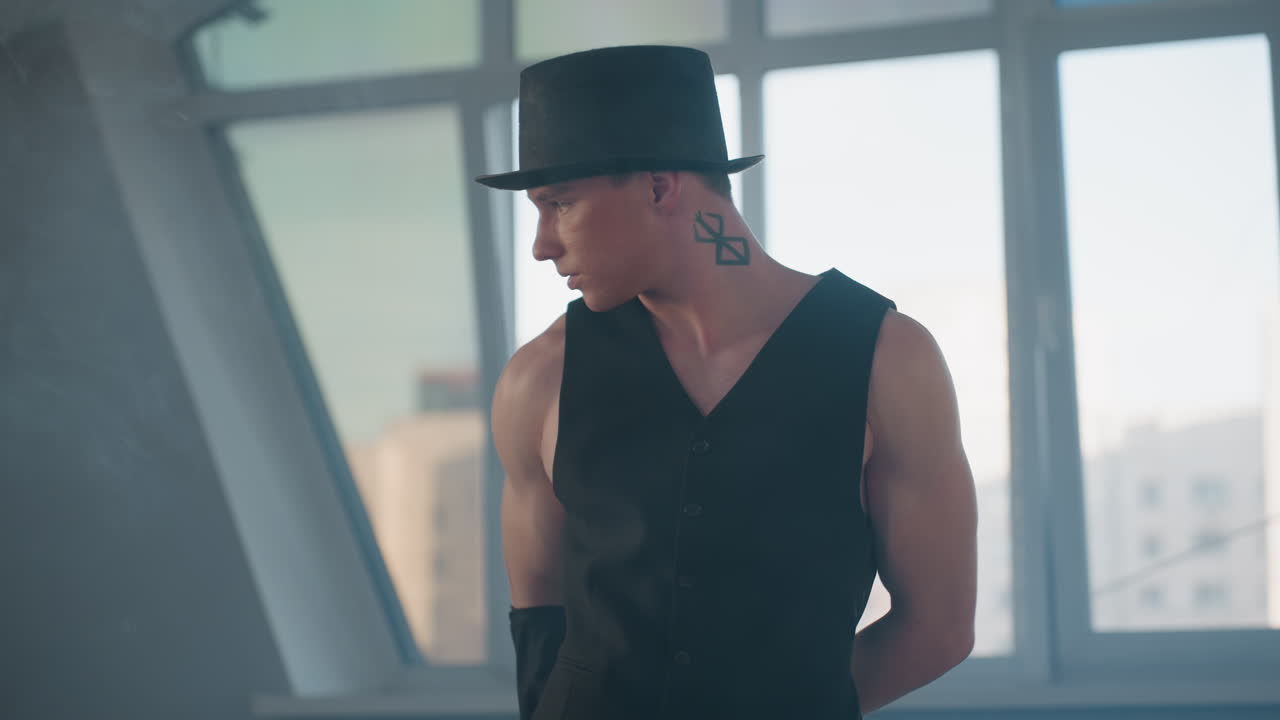 fit young student dancer in black outfit and top hat moves gracefully through smoke filled loft studio with tall windows showing blurred urban skyline with dynamic choreography and confident style