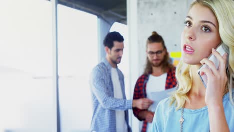 Woman-talking-on-mobile-phone-with-her-colleagues-in-background-4k