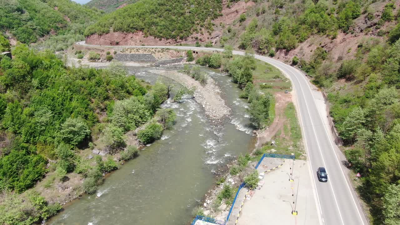 vista de avión no tripulado en albania volando sobre un paisaje verde con un río rápido y una carretera al lado con coches que pasan