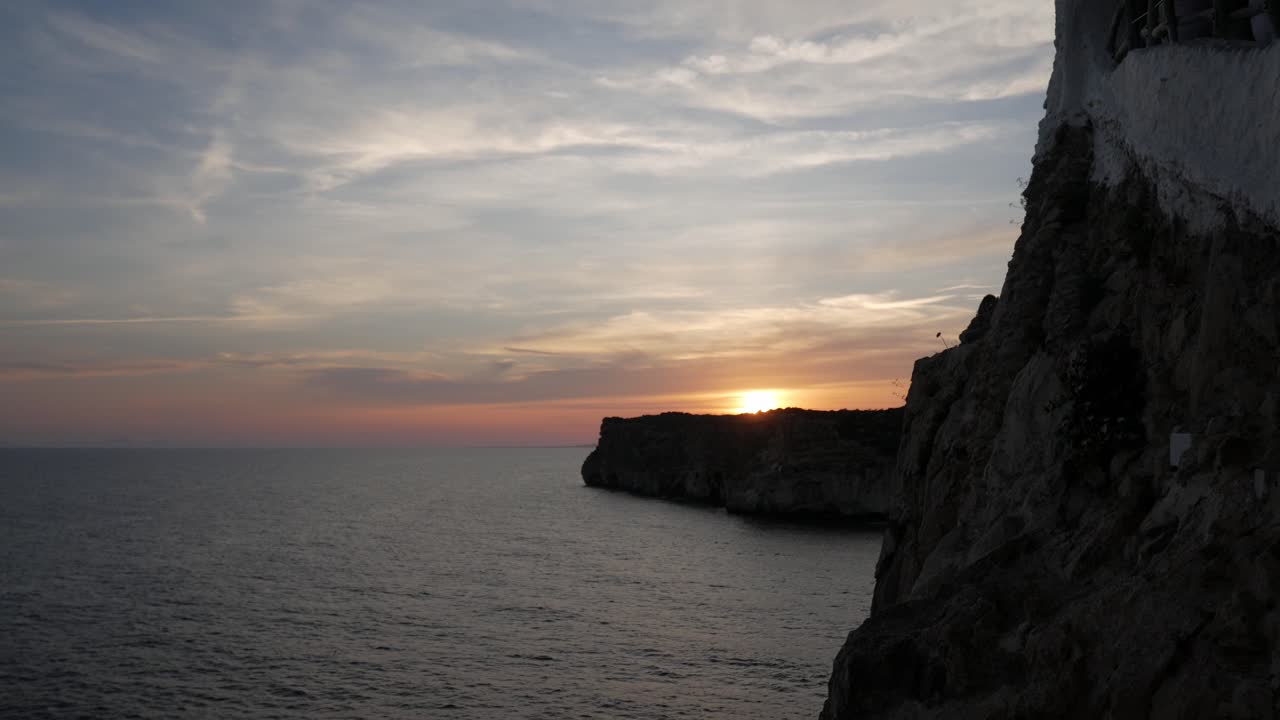 Sunset over rocky cliffs with calm ocean water at Cova D'En Xoroi, Mallorca
